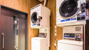 A laundry area with a front-loading washer and dryer, a water dispenser, and a smoking space sign. - APA Hotel Asakusa Kuramae Kita (Tokyo)