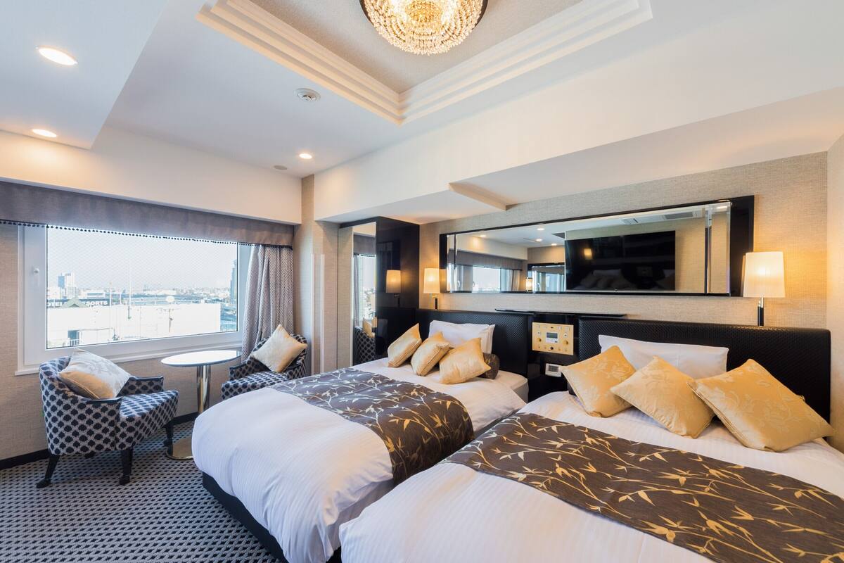 A hotel room with two beds, a seating area, a large window, and a chandelier.