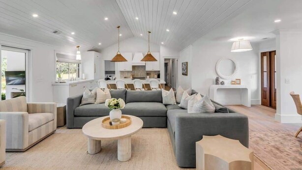 Un soggiorno moderno con un divano modulare grigio, un tavolino rotondo e una zona pranzo con mobili bianchi e illuminazione a sospensione.