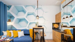 A modern living room with a blue sofa, wooden stools, and a kitchen area with wooden cabinets and a black countertop. - Comfortable Studio in Cracow | Place to Work | Close to Market Square (Kraków)