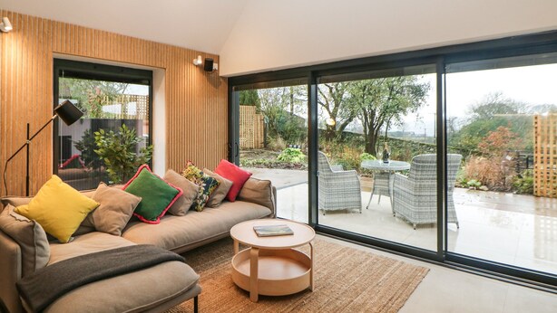 Un salon moderne avec un canapé, une table basse ronde et une grande porte vitrée donnant sur une terrasse extérieure.