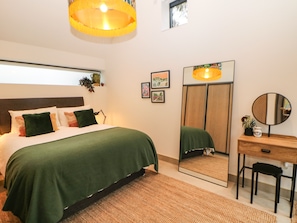 Un dormitorio con cama, escritorio, espejo y lámpara colgante.