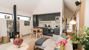 Un salon moderne avec un canapé, une table basse et une cheminée. Il y a également un coin cuisine avec des meubles sombres et un four à micro-ondes.