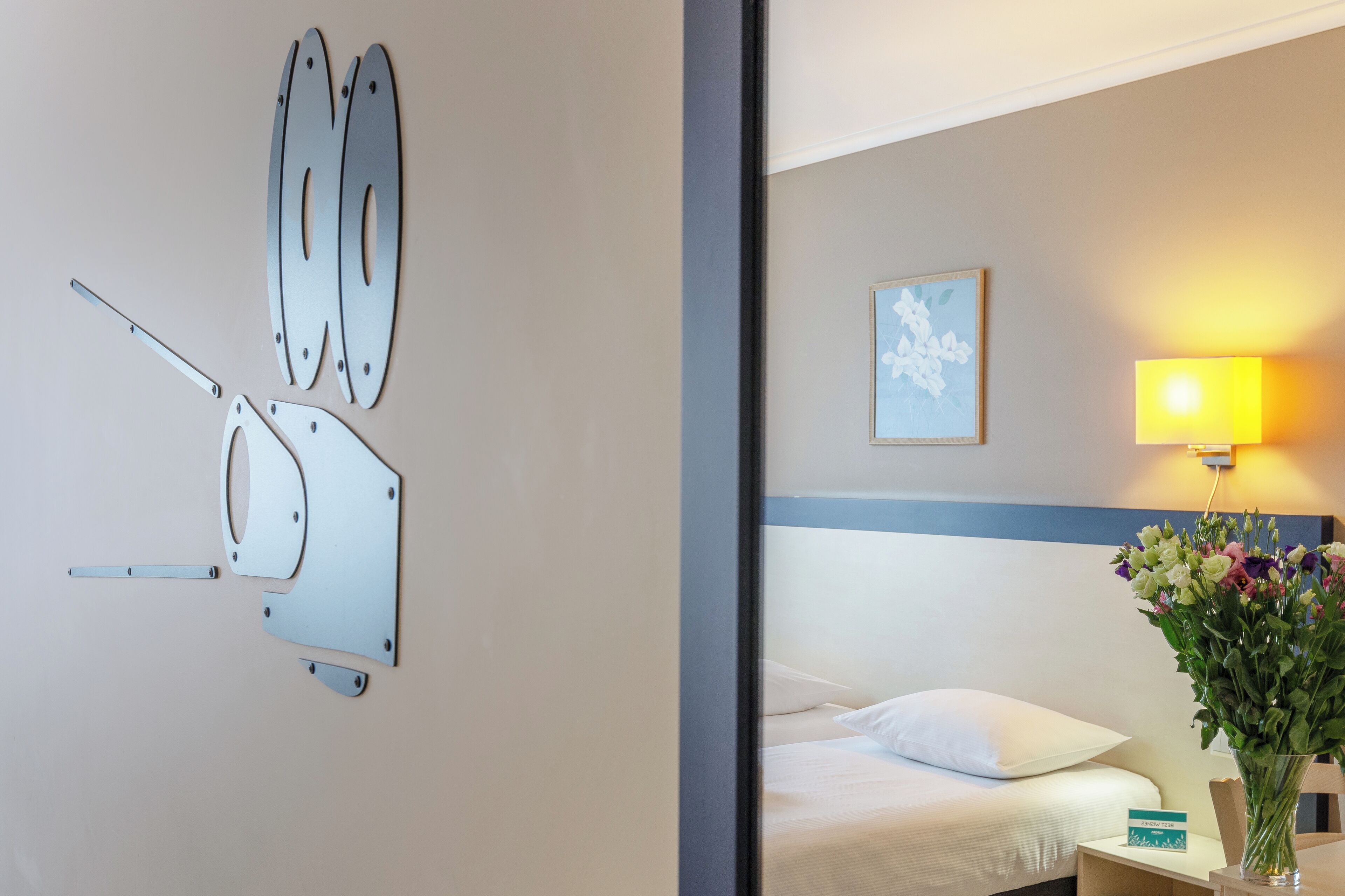 Quarto de hotel com cama, mesa de cabeceira, abajur e luminária na parede.