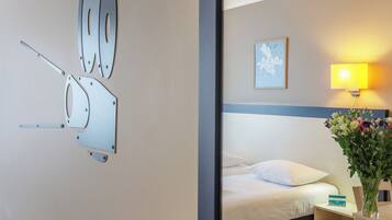 Quarto de hotel com cama, mesa de cabeceira, abajur e luminária na parede.