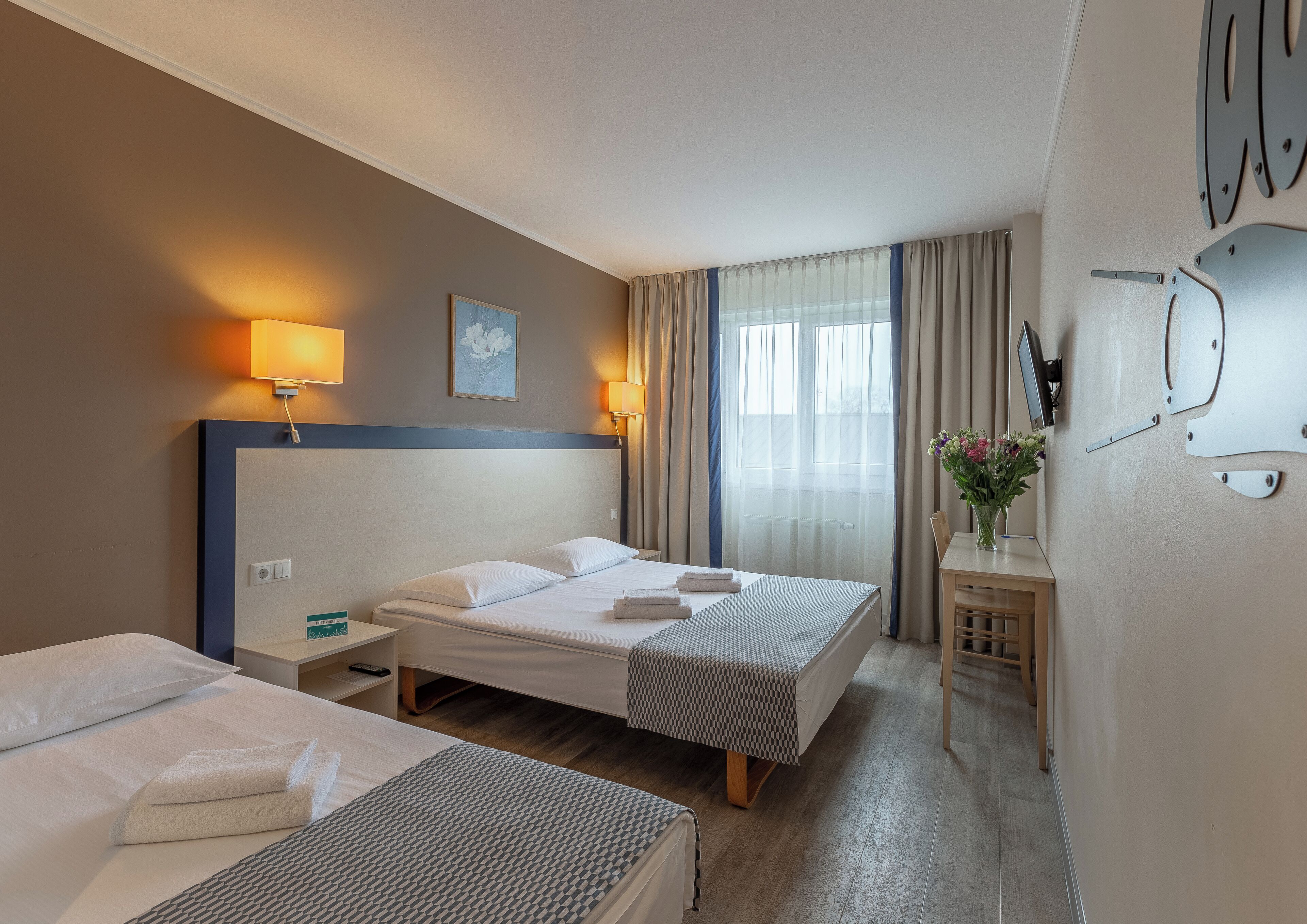 A hotel room with two beds, a desk, a chair, a TV, and a window with curtains.