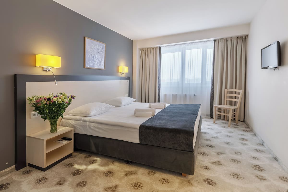 Ein Hotelzimmer mit Bett, Nachttischlampen, Fernseher, Stuhl und einem fenster mit Vorhängen.