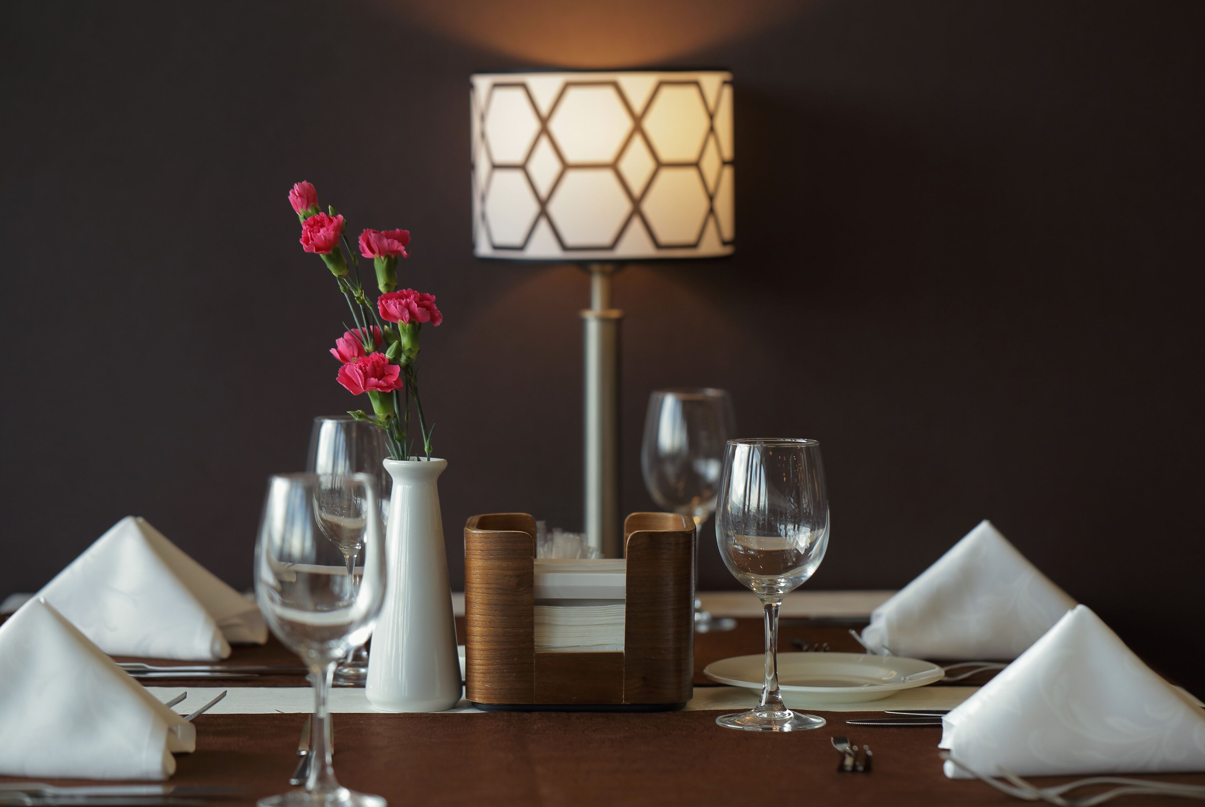 Una mesa de comedor dispuesta con servilletas blancas, un florero con flores rosas y un candelabro.