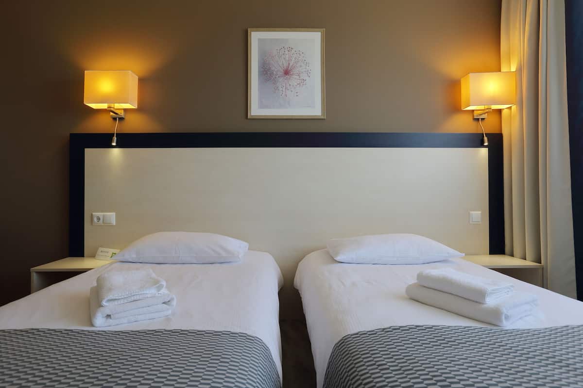 Ein Hotelzimmer mit zwei Betten, jedes mit einem ordentlich gefalteten Handtuch, einem gerahmten Kunstwerk über der Kopfteil und Wandlampen auf beiden Seiten.