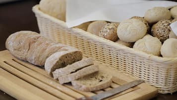 A basket of various breads and a loaf of sliced bread on a cutting board.