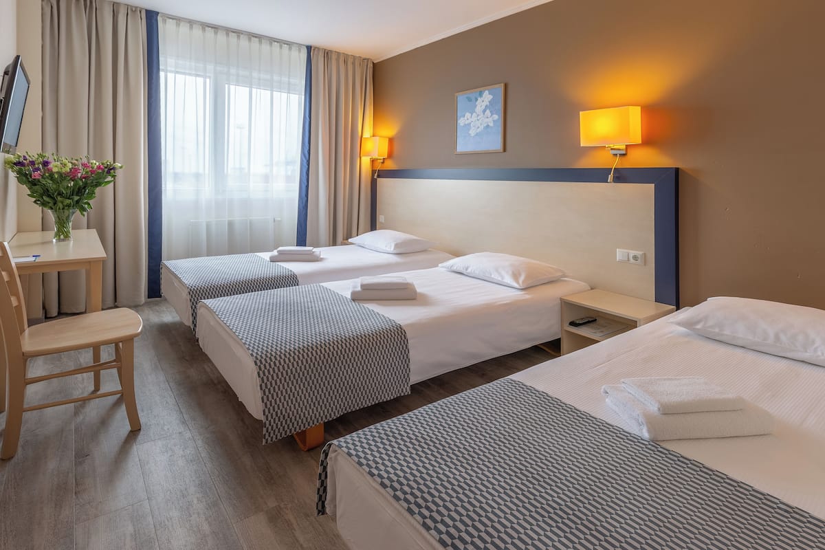 Ein Hotelzimmer mit zwei Betten, einem Schreibtisch, einem Stuhl, einem Fernseher und einem Fenster mit Vorhängen.
