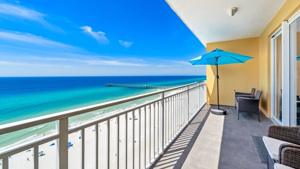 Ein Balkon mit Blick auf das Meer und einen Steg, ausgestattet mit einem Stuhl und einem Sonnenschirm.