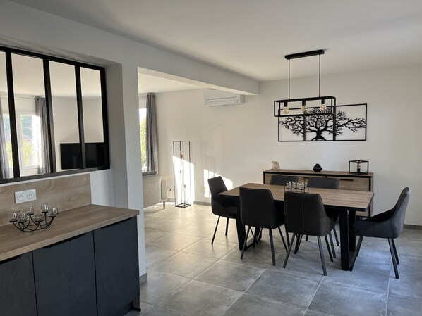A modern kitchen with a wooden countertop, a dining area with a dark wooden table and black chairs, and a large window with curtains.