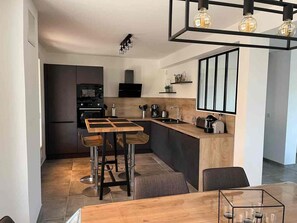 Een moderne keuken met een centraal eiland, barkrukken, een eettafel en een hanglamp.