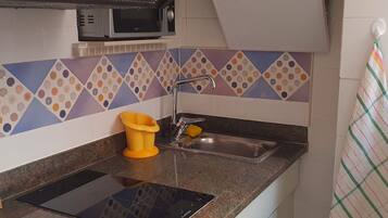 Una cocina con microondas, un lavabo y un cubo de basura amarillo.