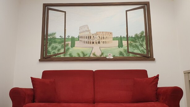 Un sofá rojo en una habitación con un cuadro enmarcado del Coliseo en la pared.