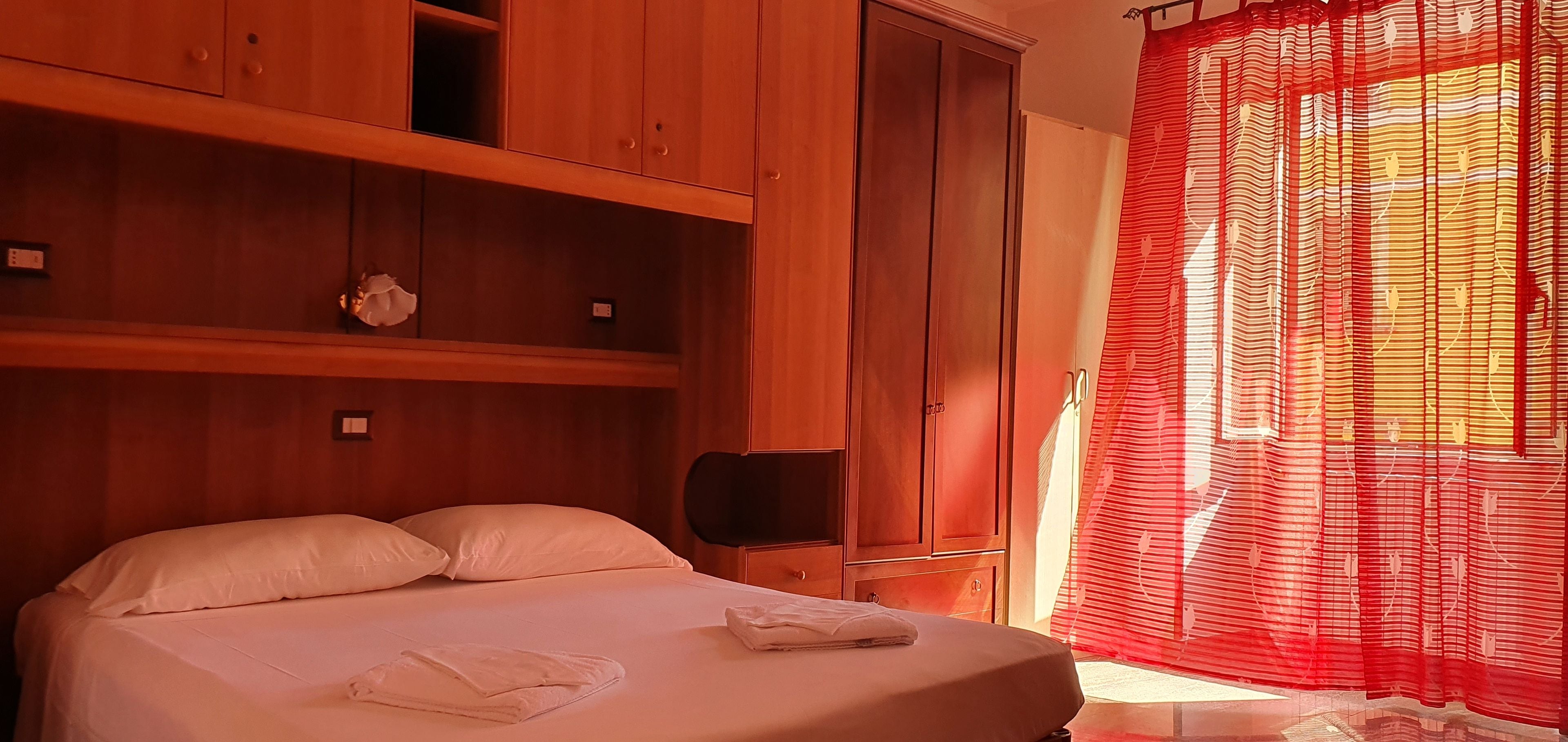 Une chambre d’hôtel avec un lit, une armoire en bois et une fenêtre avec des rideaux rouges.