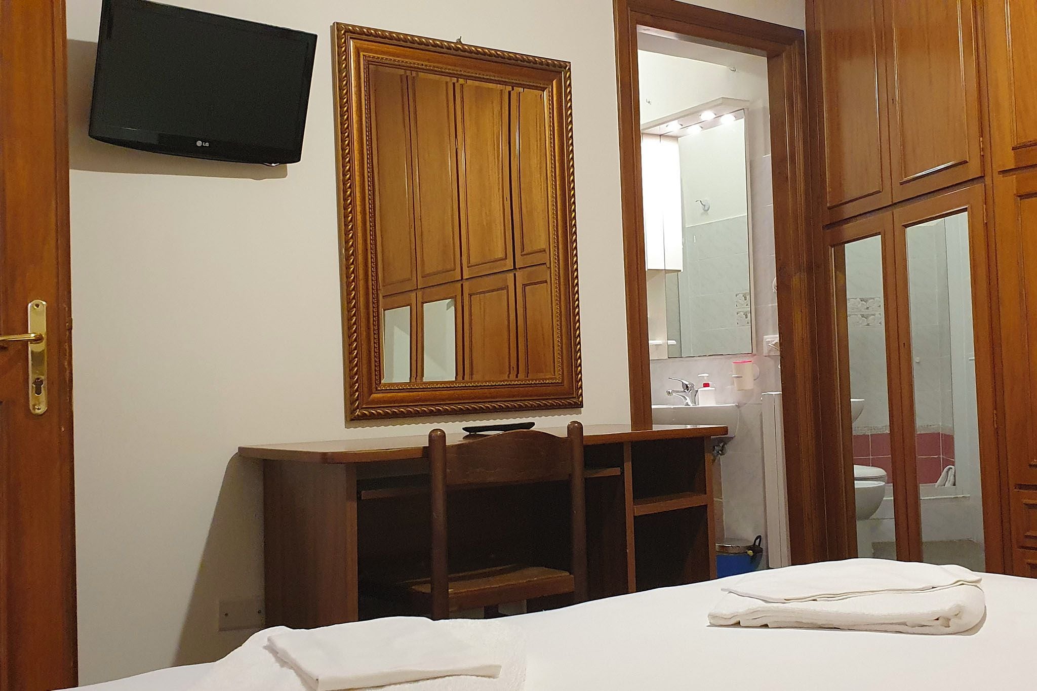 A room with a bed, a wooden cabinet, a television, and a mirror.