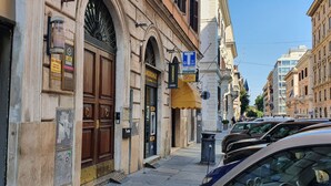 Una calle con coches aparcados, un edificio con un gran puerta de madera y un cartel de lavandería autoservicio.