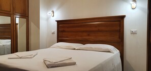 A neatly made bed with white linens and folded towels, a wooden headboard, and wall-mounted lighting fixtures. - Via Palestro 56 Apartment (Rome)