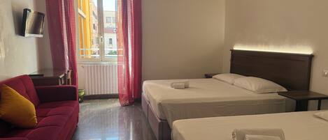 Habitació d'hotel amb llit, sofà, televisió i finestra amb cortines.