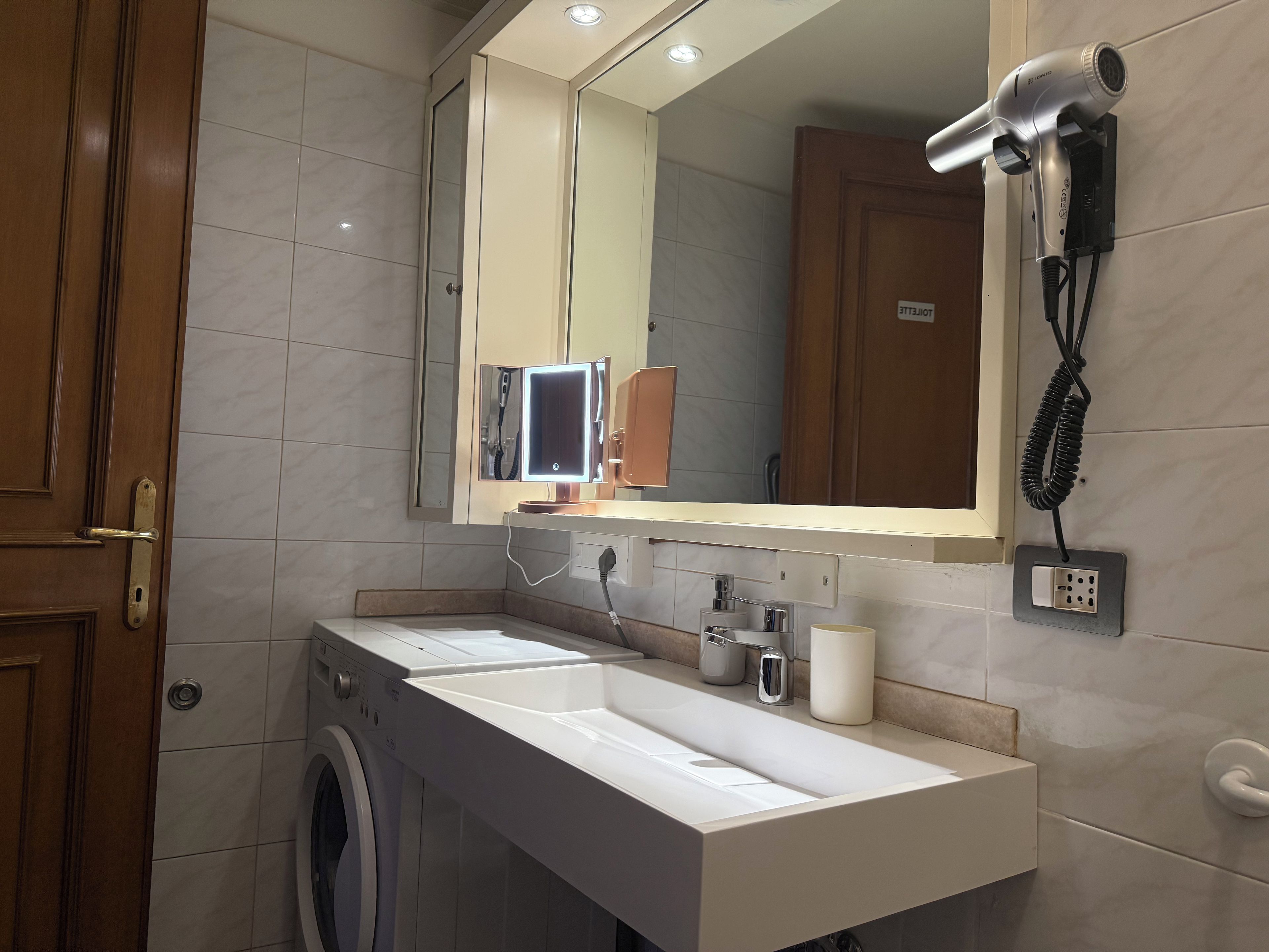 Un baño moderno con lavamanos doble, espejo, secador de pelo y lavadora.