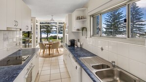 Una cucina moderna con mobili bianchi, un piano di lavoro blu e un'ampia finestra con vista sugli alberi.