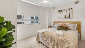 Una camera da letto con un'ampia finestra, un letto con asciugamani arrotolati e un quadro con palme.