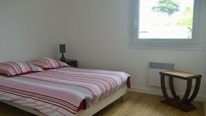 Et soveværelse med seng, natbord, lampe, vindue og radiator.
