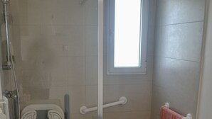 Et badeværelse med brusebad, håndvask, et vindue og en håndklædestang.