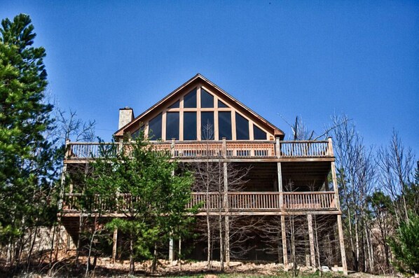Une cabane en rondins à deux étages, dotée d’un balcon au niveau supérieur et entourée d’arbres.