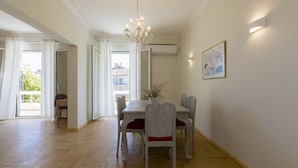 A dining area with a wooden table and chairs, a chandelier, and a painting on the wall. - The Bright Suite (Corfu)
