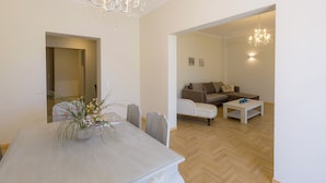 A dining area with a table and chairs, a chandelier, a sofa, and a coffee table in a modern living space. - The Bright Suite (Corfu)