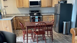 A modern kitchen with wooden cabinets, a stainless steel refrigerator, and a dining area with a table and chairs.