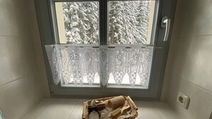 A corner of a room with a window, a lace curtain, and a wicker basket with a towel and a brush.