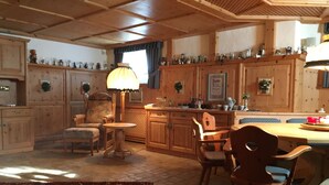 A cozy, wooden-furnished living room with a dining area, a patterned rug, and a lamp.