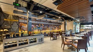 Un restaurante moderno con suelo de baldosas hexagonales, una barra central con diversos alimentos y múltiples zonas de estar con mesas y sillas.