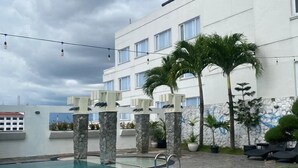 Una piscina de agua cristalina, rodeada de pilares de piedra y palmeras, con un edificio blanco al fondo.