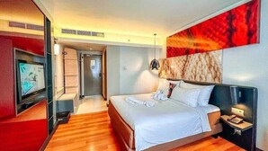 Habitación de hotel con una cama grande, televisión, escritorio con lámpara y un cuadro abstracto rojo en la pared.