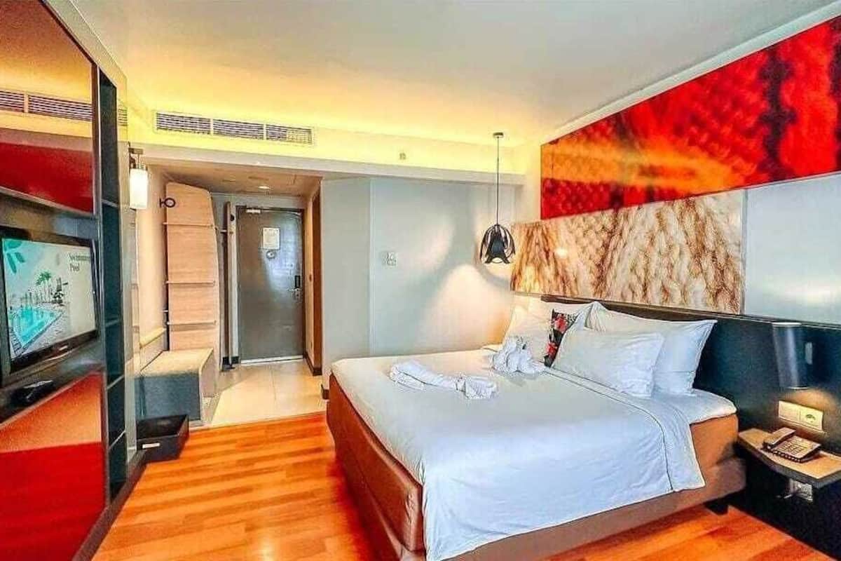Hotelkamer met een groot bed, een televisie, een bureau met lamp en een abstract rood schilderij aan de muur.