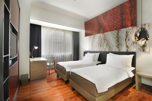 A hotel room with two beds, a desk, a chair, and a large window with curtains.
