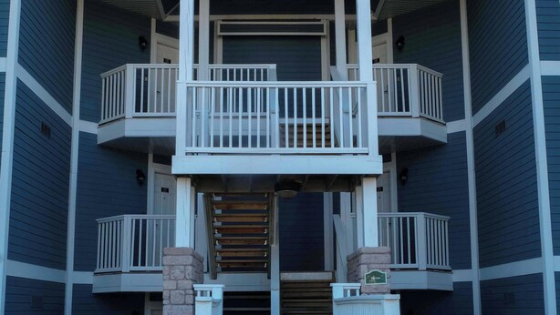 A two-story building with a balcony on the second floor, a front entrance with steps, and a small porch area. - Charming Copeland 1-bed Condo + patio + hot tub (Oro)