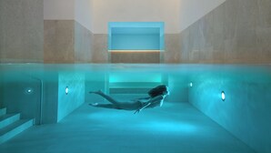 A person swimming in a modern, minimalist pool with geometric walls and recessed lighting. - Almanac Palais Vienna (Vienna)