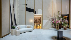 A modern lobby with a white sofa, a round table with vases, and a stone wall in the background. - Almanac Palais Vienna (Vienna)