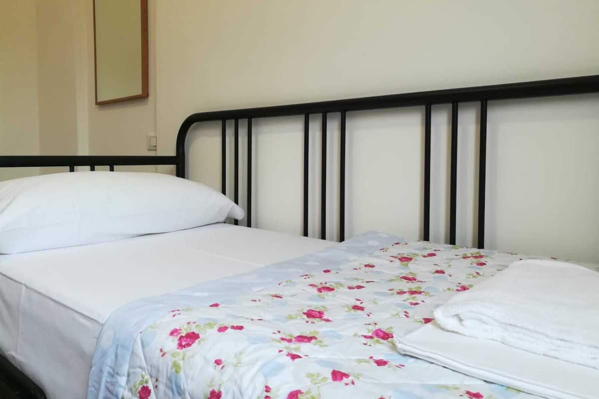 Una cama individual con estructura de metal negro, almohada blanca y colcha estampada con motivos florales.