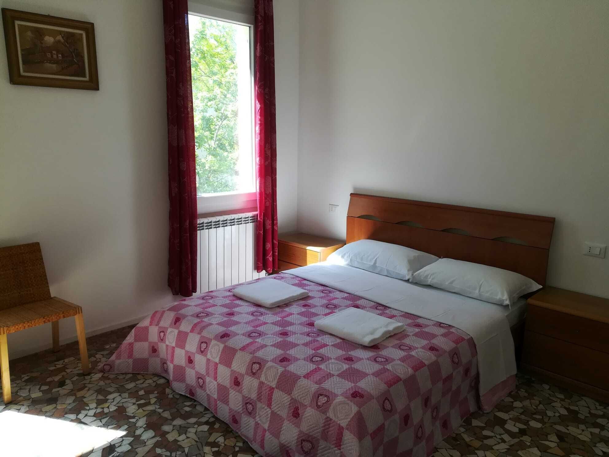 Een slaapkamer met een bed, een stoel, een nachtkastje en een raam met gordijnen.