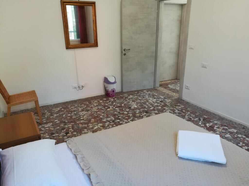 Ein Zimmer mit einem Bett, einem Sessel, einem kleinen Tisch, einem Spiegel und einer Tür.