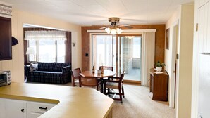 A cozy living area with a sofa, dining table, and chairs, a kitchen area with a refrigerator, and a sliding glass door leading to a balcony. - Cozy 2 bedroom cottage, lakefront private beach (Township of Branch)