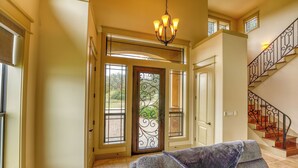 A spacious entryway with a grand staircase, a chandelier, and a view through the glass doors.