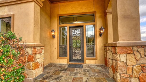 A building entrance with a stone facade, a decorative metal door, and two wall-mounted lights.